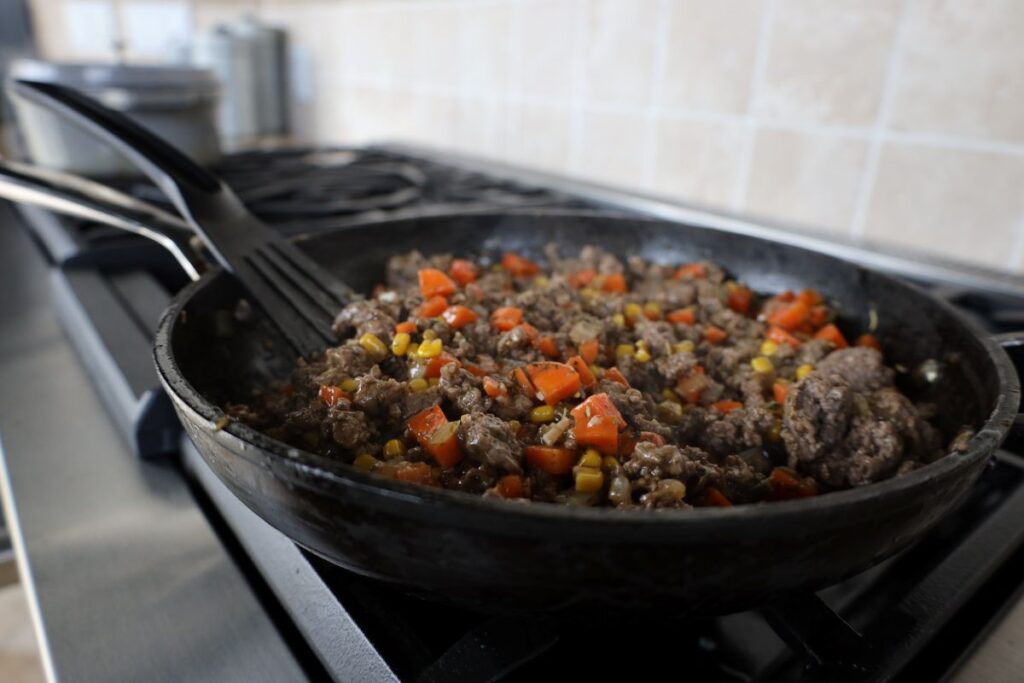 ground lamb and veggies cooking in a skillet on the stove