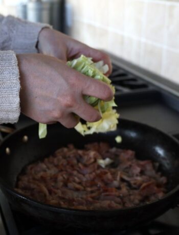 hands adding cabbage to bacon in a frying pan