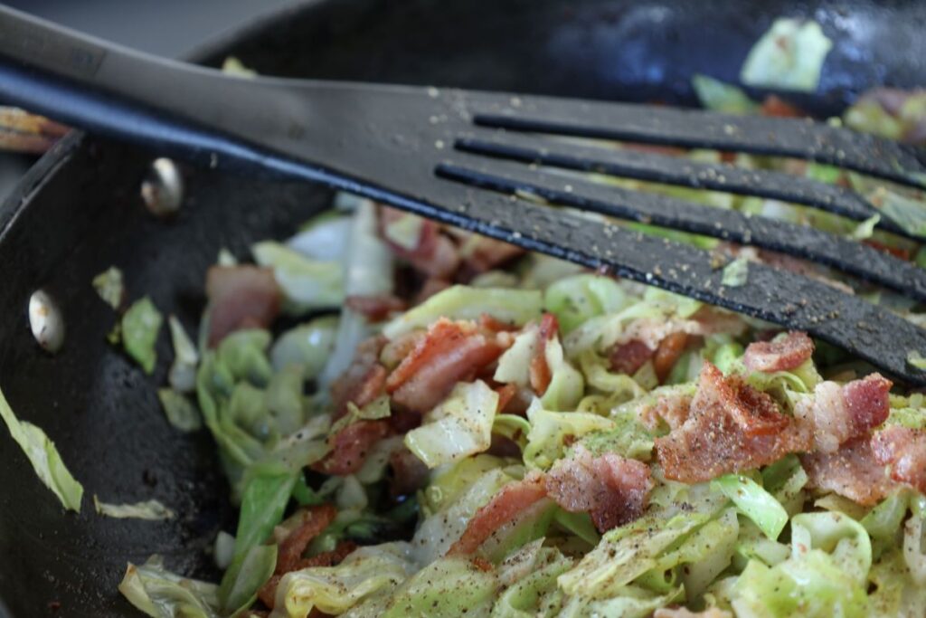 cabbage and bacon in a frying pan with salt and pepper